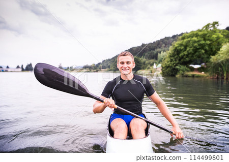 Canoeist man sitting in canoe holding paddle, in water. Concept of canoeing as dynamic and adventurous sport. Rear view, sportman looking at water surface, paddling 114499801