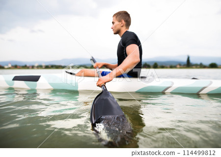 Canoeist man sitting in canoe holding paddle, in water. Concept of canoeing as dynamic and adventurous sport. Rear view, sportman looking at water surface, paddling 114499812