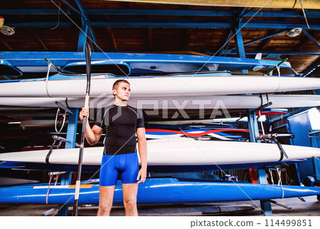 Portrat of young canoeist standing in front of stacked canoes. Concept of canoeing as dynamic and adventurous sport. 114499851