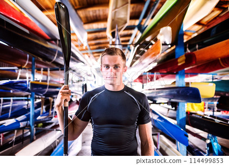 Portrat of young canoeist standing in the middle of stacked canoes. Concept of canoeing as dynamic and adventurous sport. Portrat of young canoeist standing in the middle of stacked canoes. Concept of canoeing as dynamic and adventurous sport. 114499853