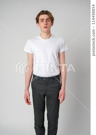 Young Man Standing in a Plain White T-Shirt Against a Gray Background Young Man Standing in a Plain White T-Shirt Against a Gray Background 114499854