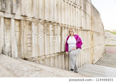 Overweight woman walking up the stairs in city park, down the stairs. Exercising outdoors for people with obesity. Overweight woman walking up the stairs in city park, down the stairs. Exercising outdoors for people with obesity. 114499855