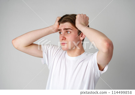 Young Man In White T-Shirt Looking Worried With Hands On Head Against Plain Background Young Man In White T-Shirt Looking Worried With Hands On Head Against Plain Background 114499858