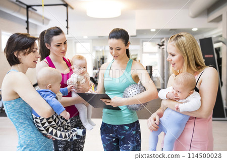 Instructor scheduling the next group exercise class. Moms staying active, working out with baby in gym. 114500028