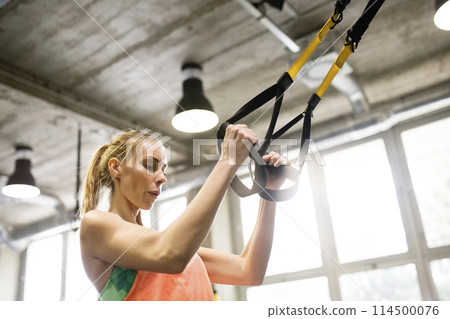 Beautiful sport woman doing suspension training, total resistance exercise. Routine workout for woman's physical and mental health. 114500076