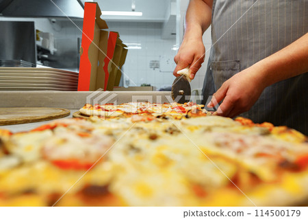 Chef Cutting Freshly Baked Pizza in a Commercial Kitchen Setting 114500179