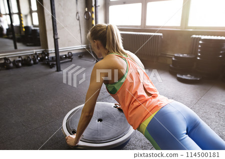 Beautiful sport woman exercising on balance ball in gym, performing pushups. Routine workout for woman's physical and mental health. Beautiful sport woman exercising on balance ball in gym, performing pushups. Routine workout for woman's physical and mental health. 114500181
