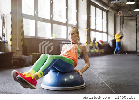 Beautiful sport woman exercising on balance ball in gym. Routine workout for woman's physical and mental health. 114500195