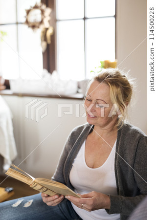 Beautiful mature woman reading book, feeling cozy and happy. Weekend activity for older woman, relaxing at home. Beautiful mature woman reading book, feeling cozy and happy. Weekend activity for older woman, relaxing at home. 114500228