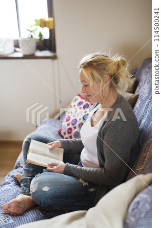 Beautiful mature woman reading book, feeling cozy and happy. Weekend activity for older woman, relaxing at home. 114500241