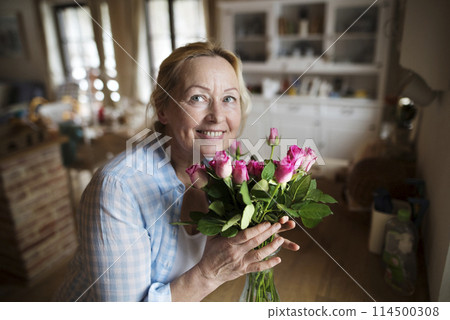 Beautiful mature woman arranging bouquet of roses in a vase, a hobby and relaxation. Older woman living alone, enjoying peaceful weekend day 114500308