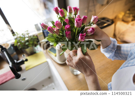Beautiful mature woman arranging bouquet of roses in a vase, a hobby and relaxation. Older woman living alone, enjoying peaceful weekend day 114500321