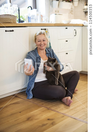 Beautiful mature woman at home, taking selfie with her cat. Older woman living alone, enjoying peaceful weekend day 114500353