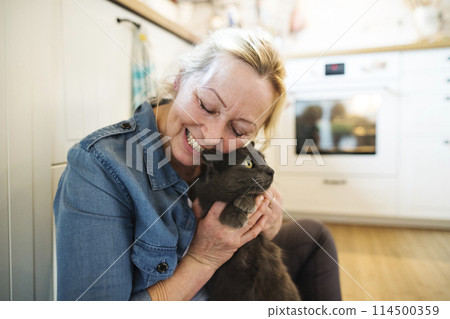 Beautiful mature woman at home, petting her cat. Older woman living alone, enjoying peaceful weekend day Beautiful mature woman at home, petting her cat. Older woman living alone, enjoying peaceful weekend day 114500359