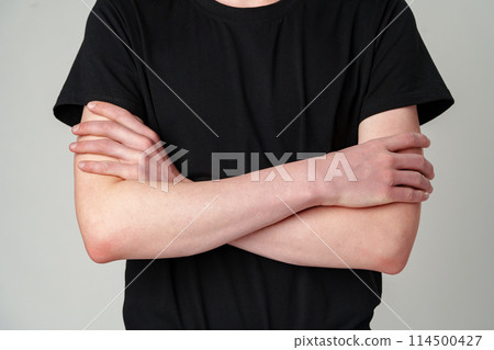 Close-Up View of a Person Standing With Arms Crossed in a Black T-Shirt Against a Grey Background Close-Up View of a Person Standing With Arms Crossed in a Black T-Shirt Against a Grey Background 114500427