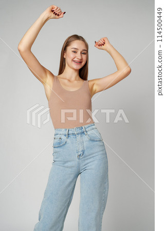 Young woman standing with her arms lifted high above her head expressing joy and triumph 114500449