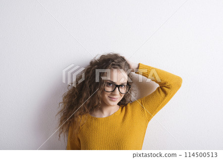 Portrait of a gorgeous teenage girl with curly hair and eyeglasses. Studio shot, white background with copy space 114500513