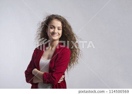 Portrait of a gorgeous teenage girl with curly hair in red blazer. Studio shot, white background with copy space 114500569