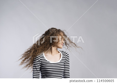 Portrait of a gorgeous teenage girl with curly hair, blowing in wind. Studio shot, white background with copy space 114500605