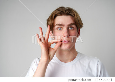 Young Man Performing Hand Gesture Near Face Against Plain Background 114500881