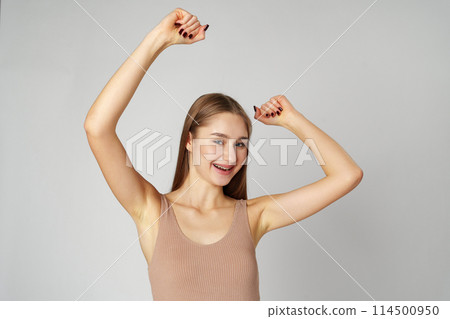 Young woman standing with her arms lifted high above her head expressing joy and triumph 114500950