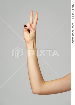 Female hand showing two fingers up on gray background Female hand showing two fingers up on gray background 114501207