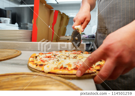 Chef Cutting Freshly Baked Pizza in a Commercial Kitchen Setting Chef Cutting Freshly Baked Pizza in a Commercial Kitchen Setting 114501259