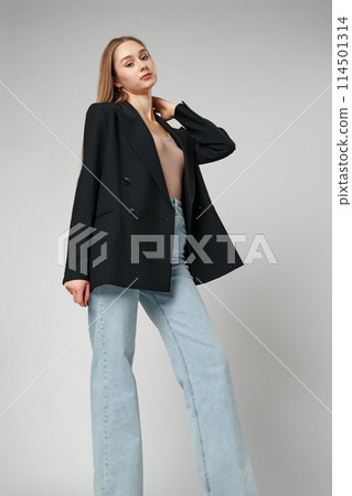 Young Woman Wearing Black Jacket and Jeans posing on gray background studio shot . Young Woman Wearing Black Jacket and Jeans posing on gray background studio shot . 114501314
