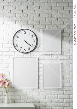 Minimalist White Wall Decor Featuring a Clock and Blank Photo Frames 114501582