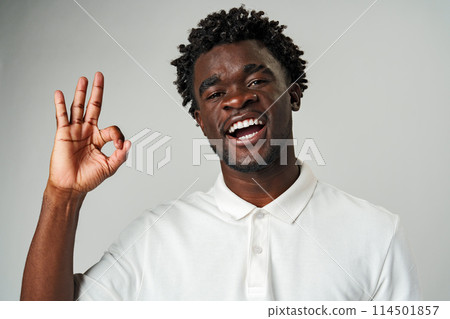 African Man in White Shirt Making Peace Sign against Gray Background African Man in White Shirt Making Peace Sign against Gray Background 114501857