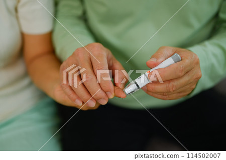 Cropped shot of senior husband helping his wife checking blood sugar level at home. Health care concept Cropped shot of senior husband helping his wife checking blood sugar level at home. Health care concept 114502007