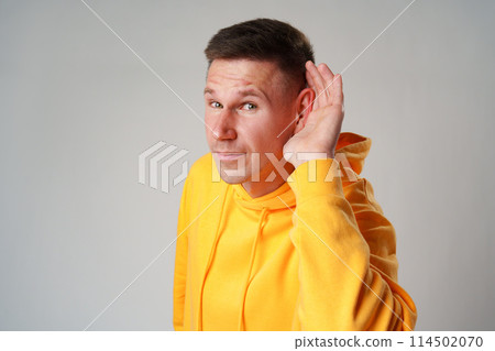 Portrait of young casual man with hand on ear who overhears on gray background Portrait of young casual man with hand on ear who overhears on gray background 114502070