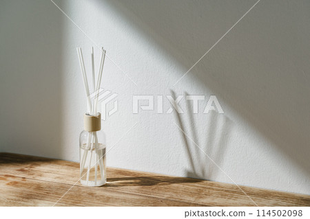 Sunlit Diffuser Bottle With Reeds Casting Shadows on a White Wall Sunlit Diffuser Bottle With Reeds Casting Shadows on a White Wall 114502098