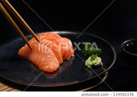 Fresh salmon sashimi on black plate with wasabi and parsley leaf. Japanese food style Fresh salmon sashimi on black plate with wasabi and parsley leaf. Japanese food style 114502156