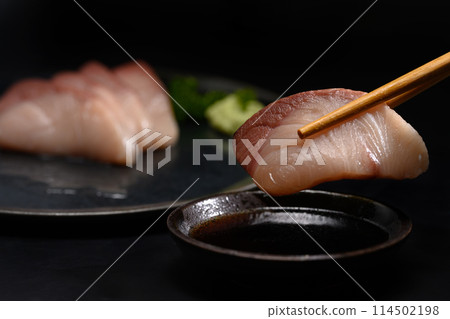 Closeup chopsticks with Yellow tail fish or Hamachi Sashimi dipping into soy sauce 114502198
