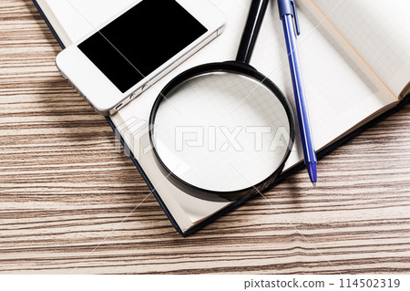 Assorted Office Supplies with Mobile Phone and Magnifying Glass on Wooden Table Assorted Office Supplies with Mobile Phone and Magnifying Glass on Wooden Table 114502319