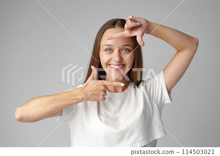 Young woman making frame with fingers on a gray background 114503021