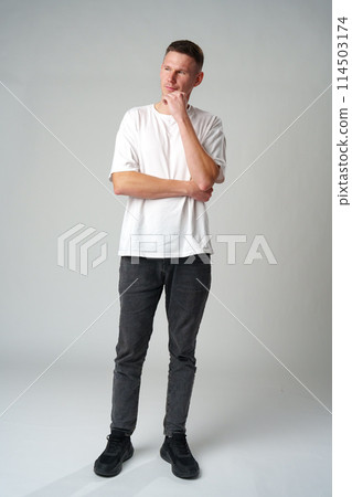 Thoughtful caucasian young male touching chin with hand thinking on gray background 114503174