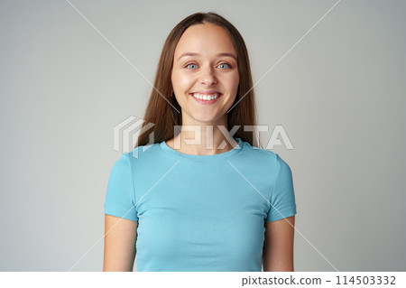 Portrait of smiling young woman in blue T-shirt on gray background Portrait of smiling young woman in blue T-shirt on gray background 114503332