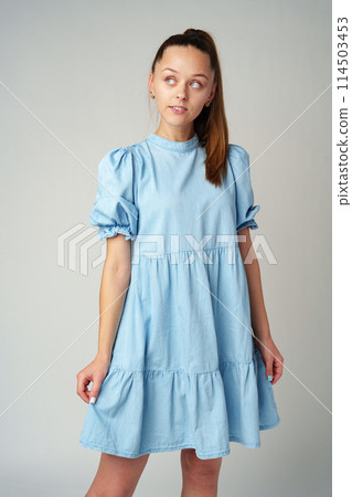 Young happy smiling woman in a light blue dress on a gray background 114503453
