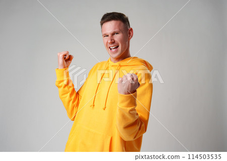 Portrait of a satisfied young man celebrating success over gray background 114503535