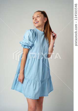 Young happy smiling woman in a light blue dress on a gray background Young happy smiling woman in a light blue dress on a gray background 114503546