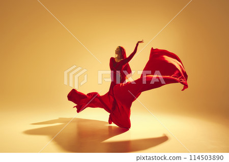 Artistic and deep performance Woman, female dancer in flowing red dress dancing against golden color background Artistic and deep performance Woman, female dancer in flowing red dress dancing against golden color background 114503890