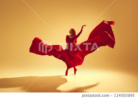 Artistic and deep performance Woman, female dancer in flowing red dress dancing against golden color background Artistic and deep performance Woman, female dancer in flowing red dress dancing against golden color background 114503895