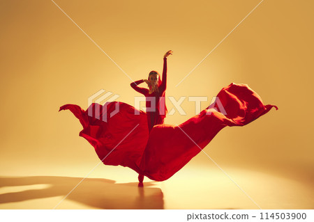 Artistic and deep performance Woman, female dancer in flowing red dress dancing against golden color background Artistic and deep performance Woman, female dancer in flowing red dress dancing against golden color background 114503900