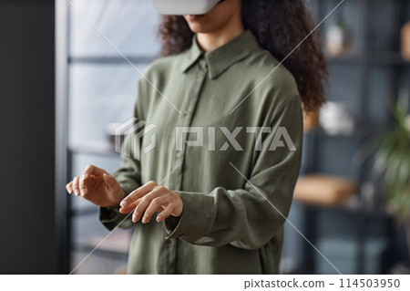 Selective focus shot of unrecognizable girl in VR headset standing indoors typing on virtual keyboard in air, copy space 114503950