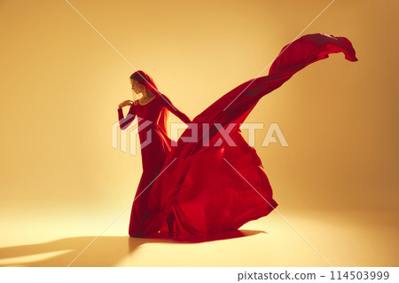 Passion in motion. Beautiful woman, dancer in flowing elegant red dress making powerful performance against sand color background 114503999