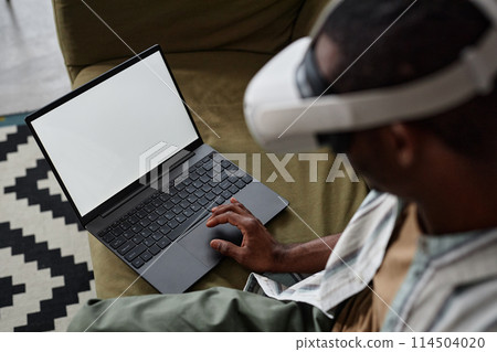 High angle view of unrecognizable Black man wearing VR headset using laptop, copy space High angle view of unrecognizable Black man wearing VR headset using laptop, copy space 114504020