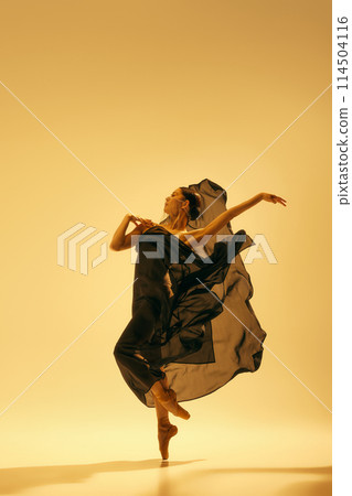 Full-length of beautiful female ballet dancer making creative performance, dancing in flowing black costume against sand color background Full-length of beautiful female ballet dancer making creative performance, dancing in flowing black costume against sand color background 114504116