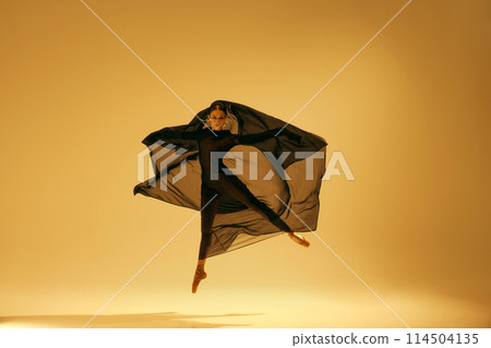 Artistic dance expression. Beautiful ballerina with golden accessories, in black costume dancing against yellow studio background 114504135